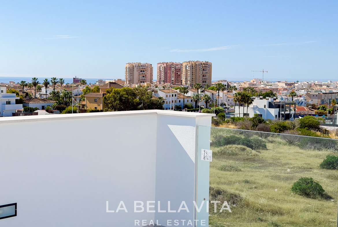 Panoramic sunlit terrace of new build villa in Aguas Nuevas, Torrevieja, overlooking lush greenery and city skyline.