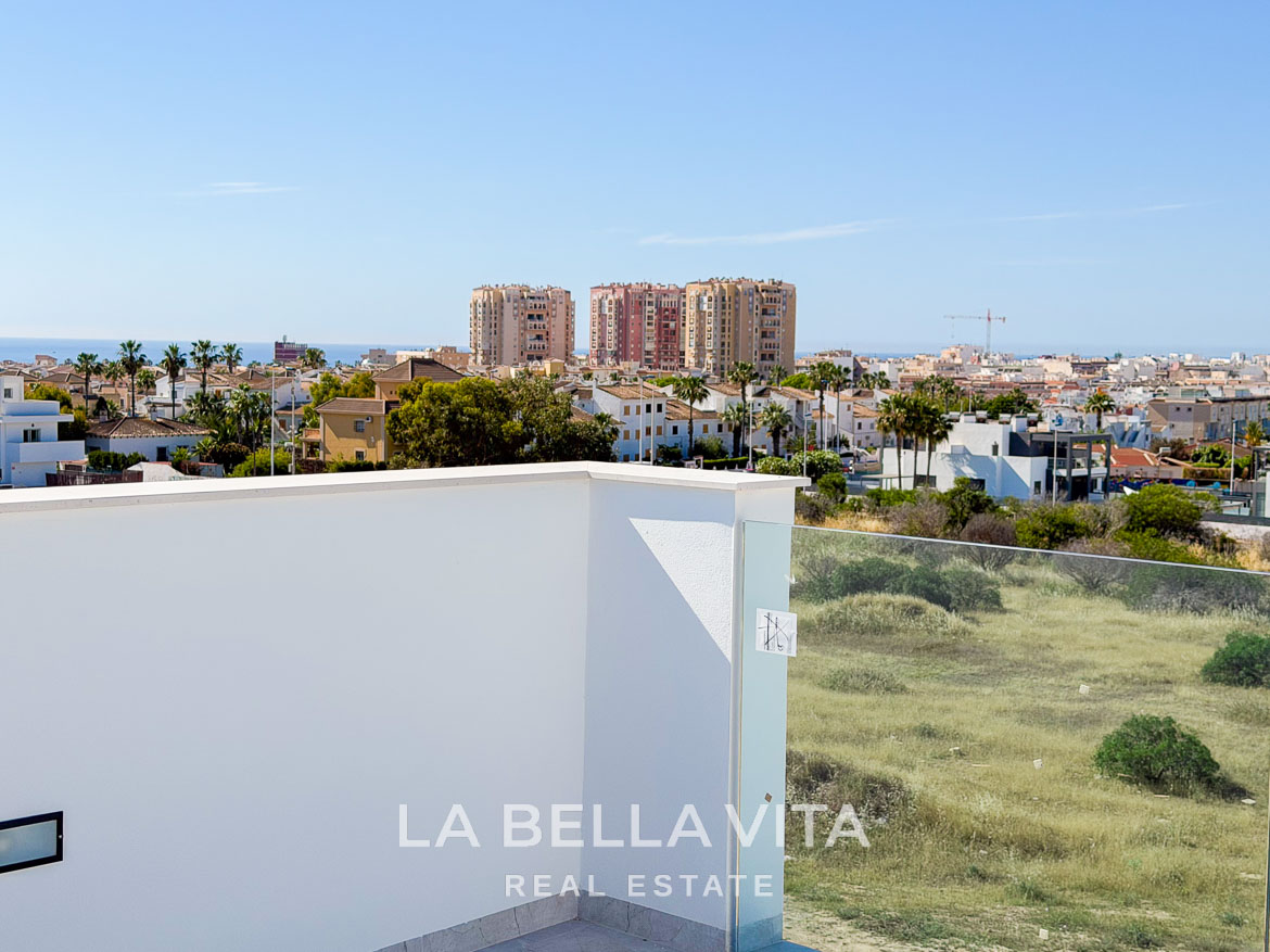 Panoramic sunlit terrace of new build villa in Aguas Nuevas, Torrevieja, overlooking lush greenery and city skyline.