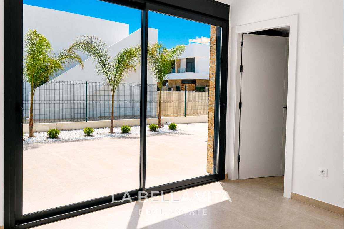 Bright open-plan interior with sleek sliding doors opening to a sunlit terrace and palm-lined courtyard of a new single-storey villa in Los Montesinos, Costa Blanca