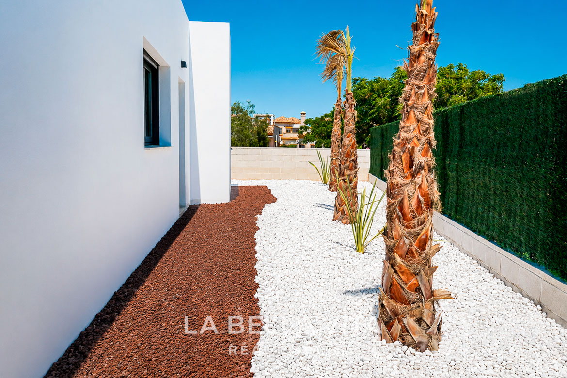 Modern single-storey villa exterior in Los Montesinos with landscaped garden featuring palm trees and contrasting stone pathways