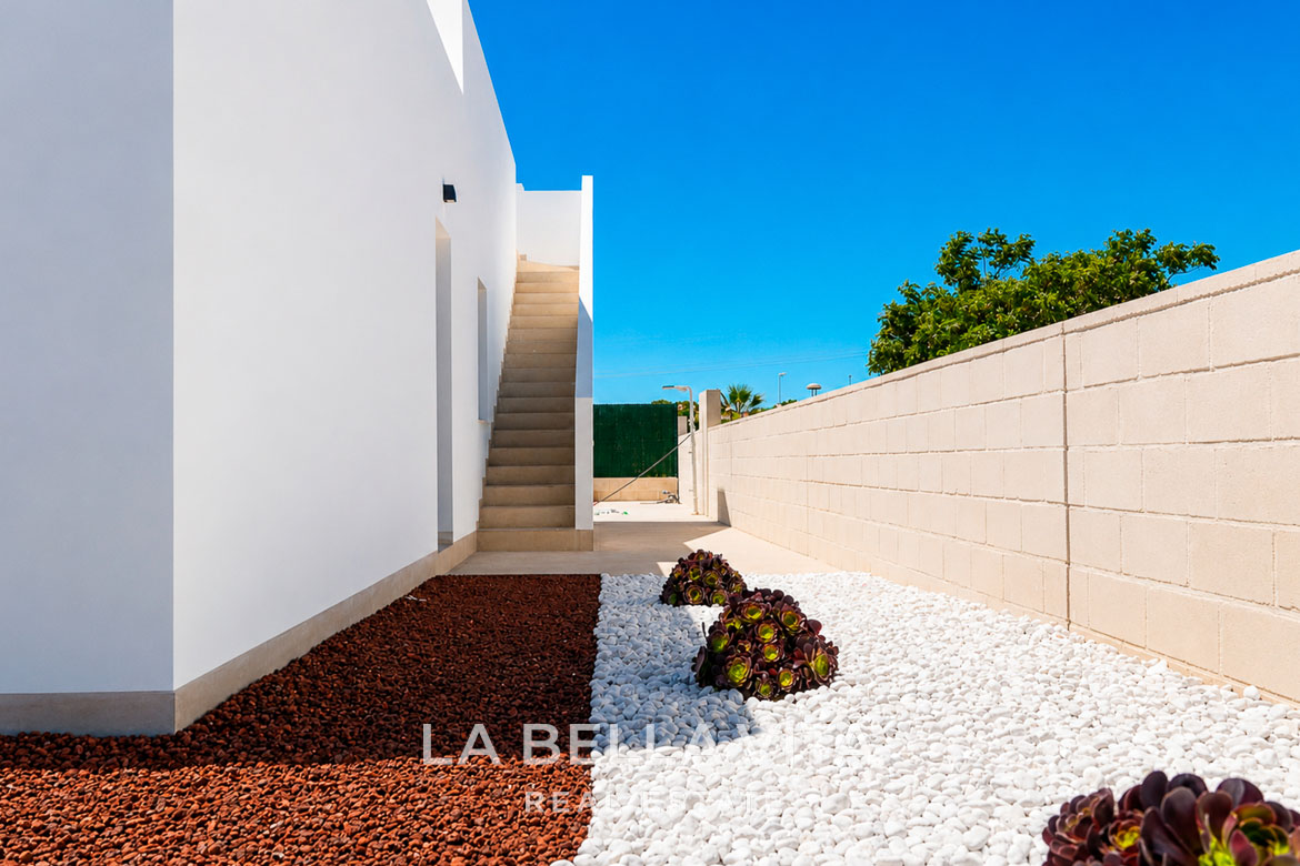 Modern single-storey villa exterior in Los Montesinos with landscaped garden featuring vibrant white and red stones.