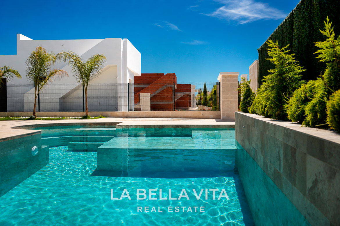 Sunlit private pool with clear turquoise water beside modern single-storey villa under construction in Los Montesinos, Costa Blanca