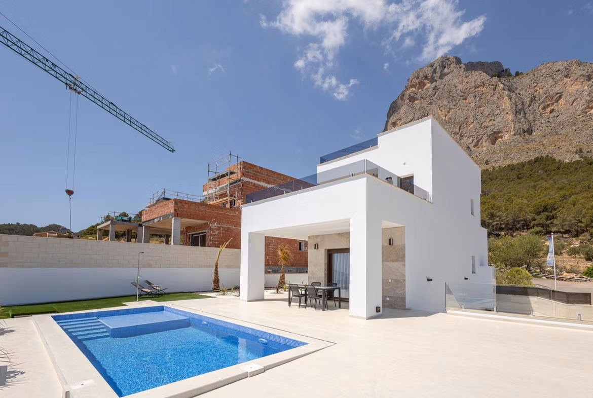 Stunning-New-Build-Villas-in-Polop-with-Sea-Views-3 New build villa in Polop with a private pool, outdoor dining area, and mountain views under a clear blue sky.
