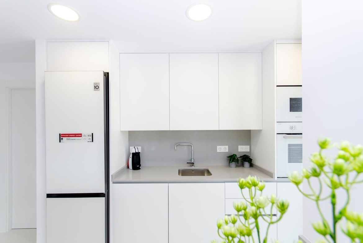 Modern kitchen with white cabinetry and built-in appliances in stylish new build semi-detached villa, Vistabella Golf Resort