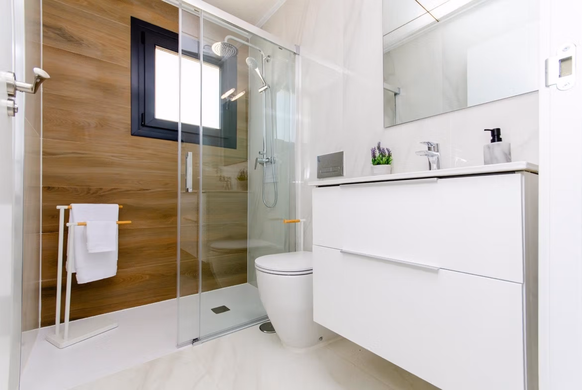 Luxury-New-Build-Semi-Detached-Villas-at-Vistabella-Golf-Resort-24 Modern bathroom with glass shower, wooden accent wall, and white vanity in a semi-detached villa at Vistabella Golf Resort.