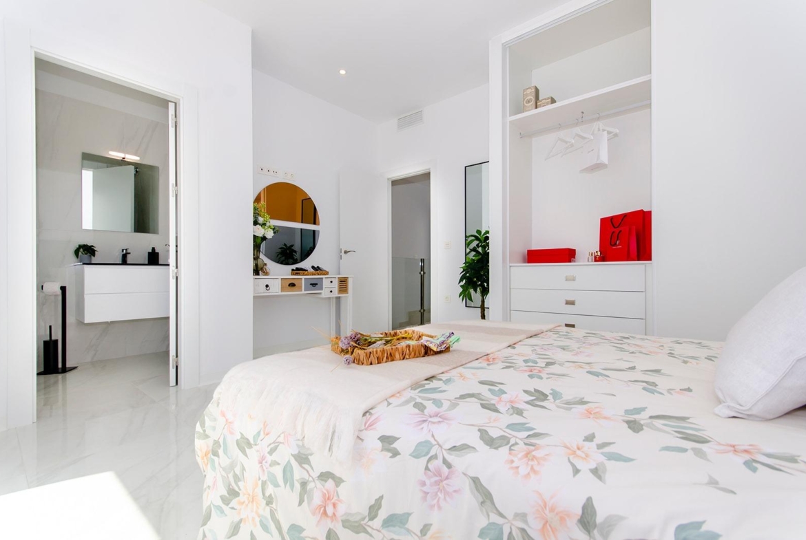 Bright bedroom with floral bedding, open bathroom door, and built-in wardrobe in new semi-detached villa at Vistabella Golf Resort.
