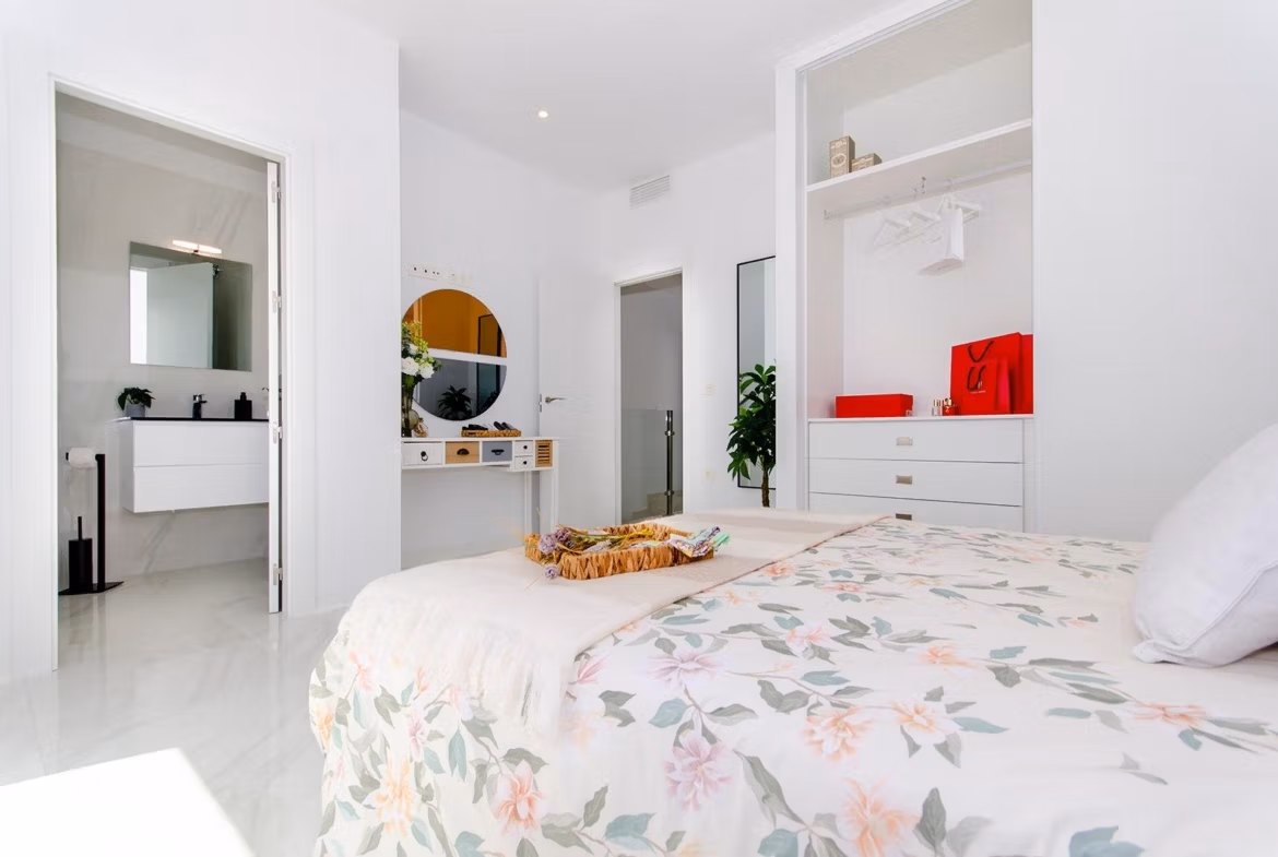Luxury-New-Build-Semi-Detached-Villas-at-Vistabella-Golf-Resort-29 Bright bedroom with floral bedding, open bathroom door, and built-in wardrobe in new semi-detached villa at Vistabella Golf Resort.