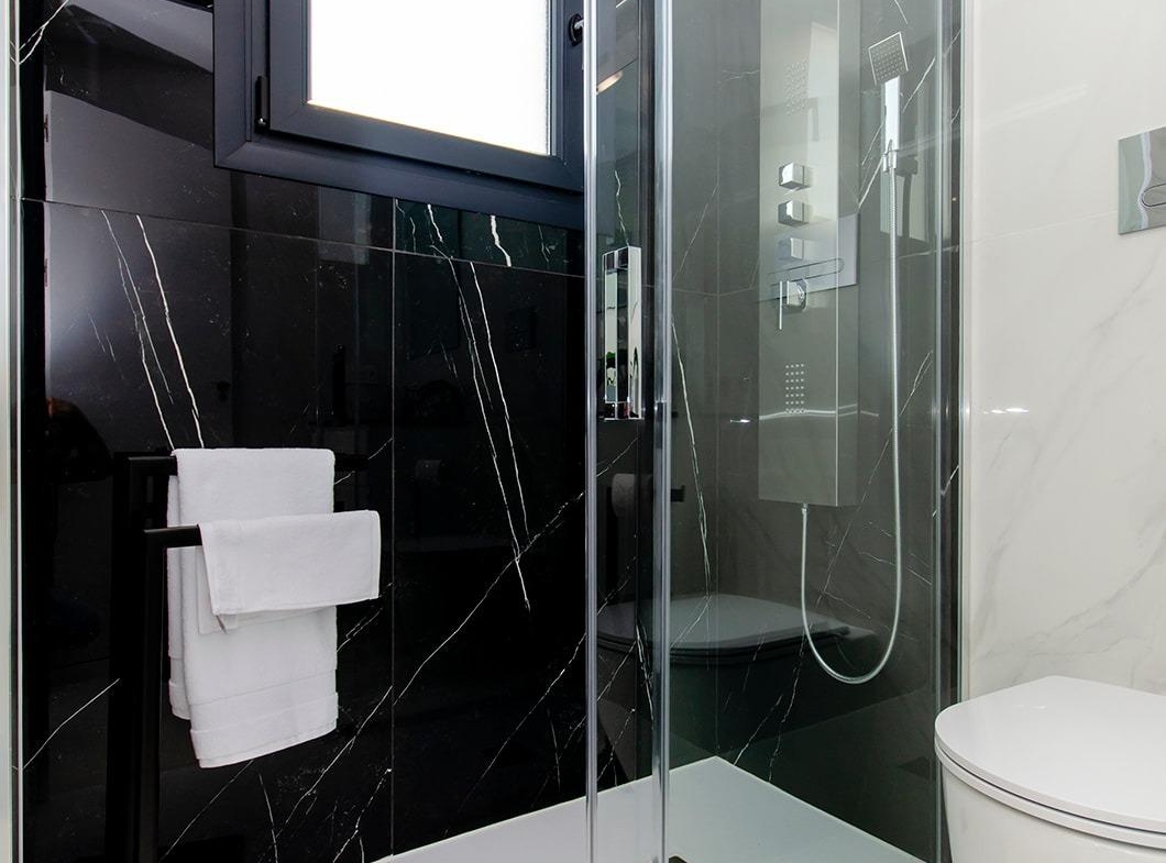 Modern bathroom with glass shower, black marble wall, and white fixtures in a new build semi-detached villa at Vistabella Golf Resort