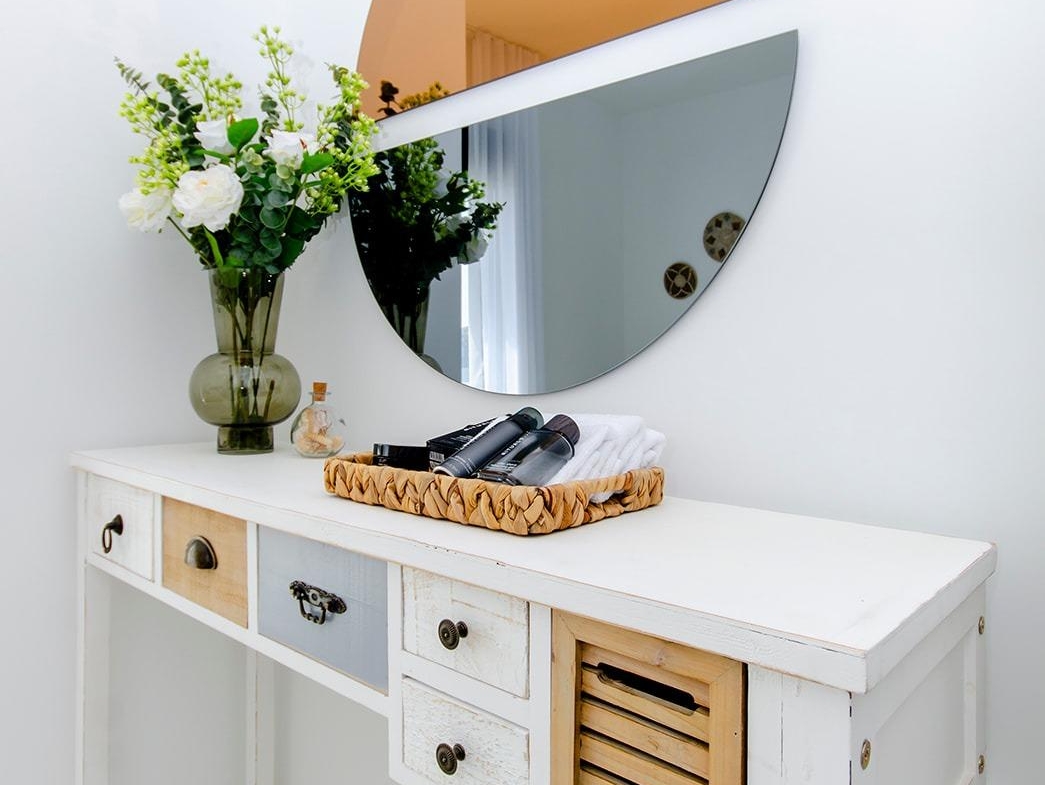 White wooden console table with decorative items and a round two-tone mirror in a semi-detached villa interior at Vistabella Golf Resort
