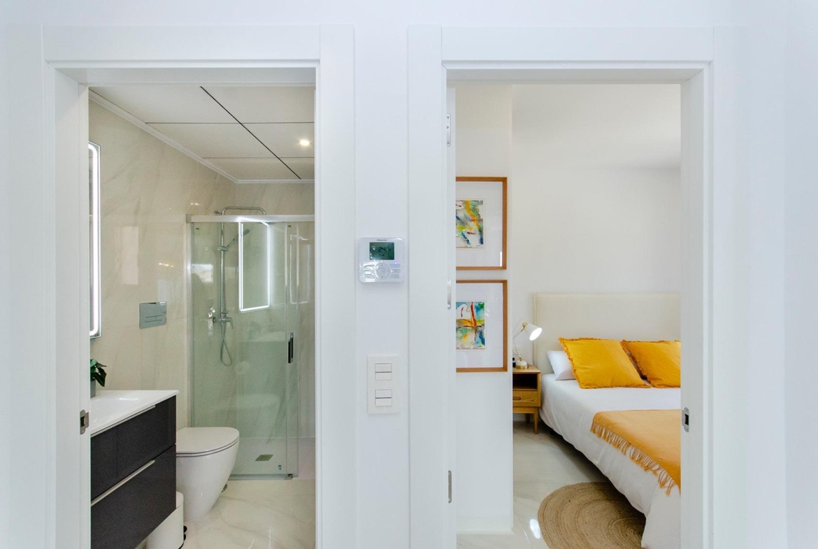 Bathroom with glass shower and bedroom with yellow accents in a new build semi-detached villa in Vistabella Golf Resort
