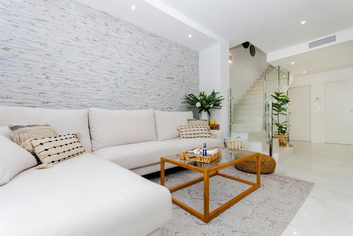 Bright living room with white sofa, glass coffee table, and staircase in a semi-detached villa in Vistabella Golf Resort.