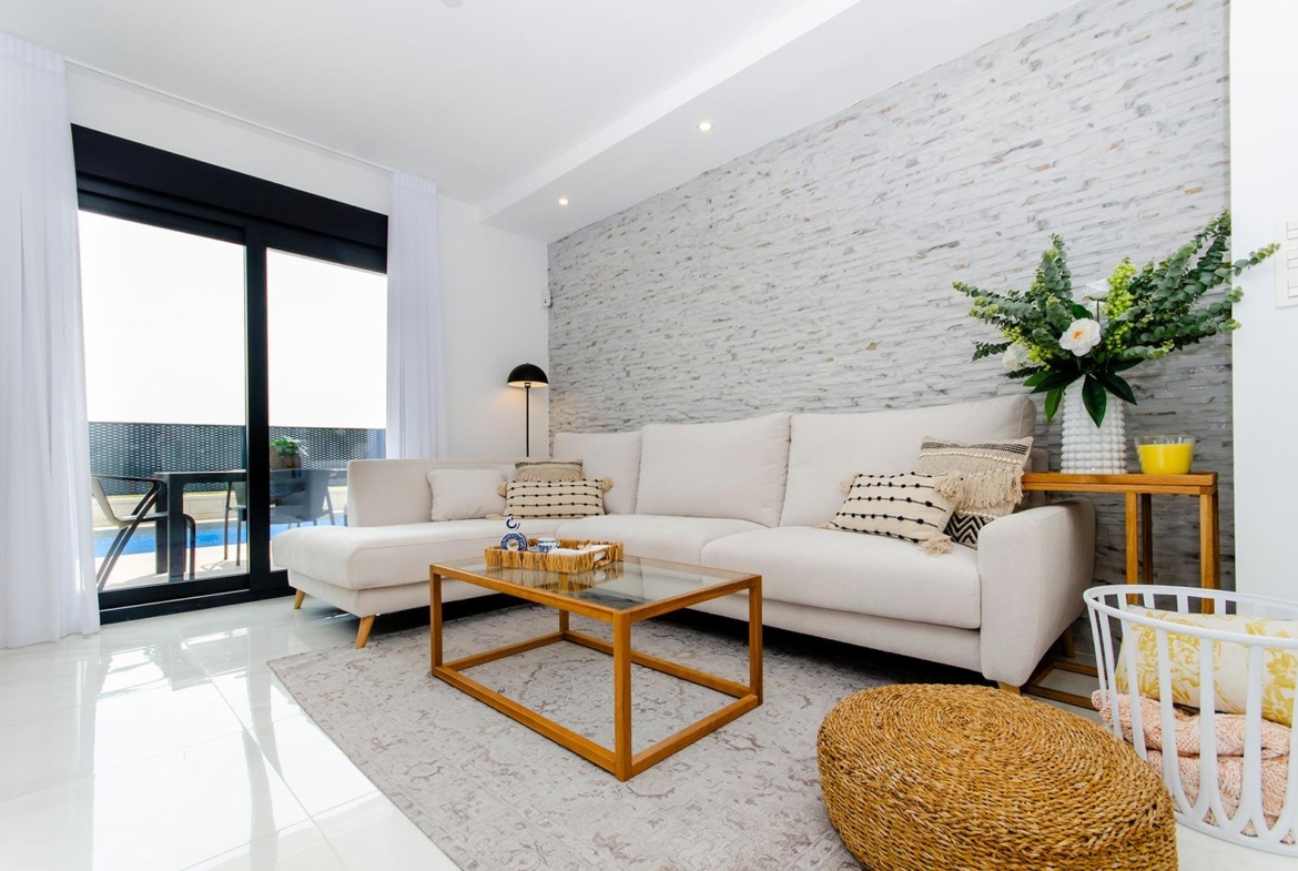 Bright living room with white sofa and glass doors opening to pool in a new semi-detached villa at Vistabella Golf Resort
