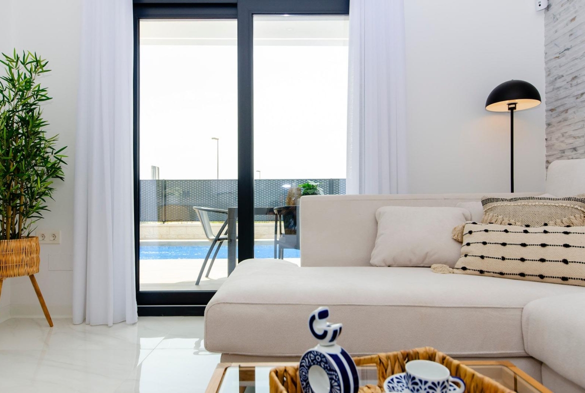Bright living room interior with modern sofa and view of private pool in new semi-detached villa at Vistabella Golf Resort