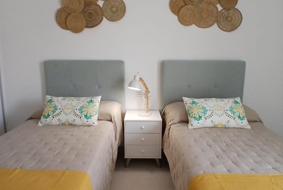 Twin beds with yellow throws and decorative pillows in a bedroom of a new build quad villa in Bigastro, Alicante.