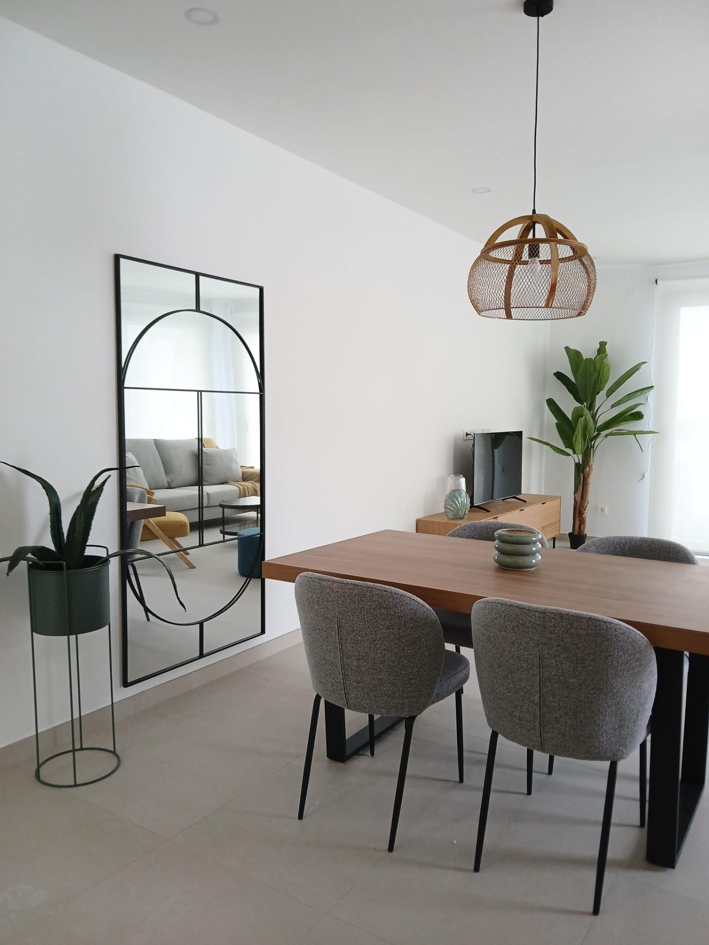 Modern-New-Build-Quad-Villas-in-Bigastro-Alicante-2 Modern dining area with wooden table, four gray chairs, decorative plants, and large mirror in Bigastro quad villa interior