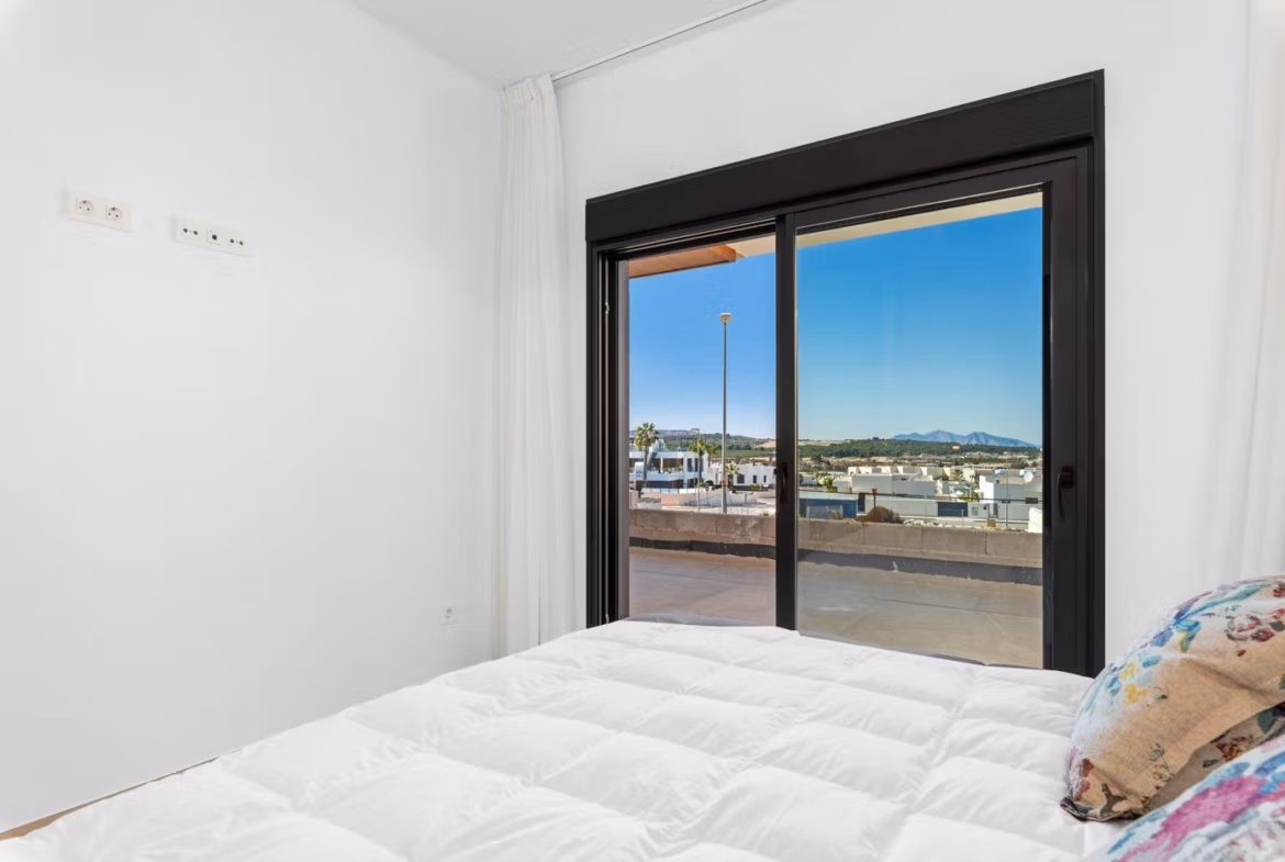 Bright bedroom with white bedding and sliding glass doors leading to a terrace in a new 2-bedroom apartment in Benijofar, Alicante.