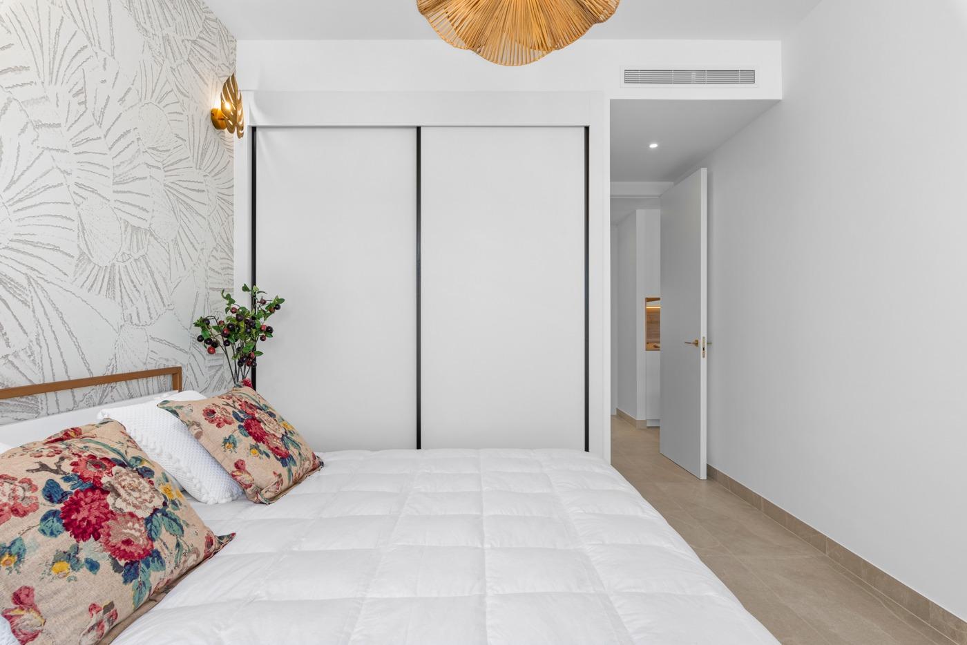 Bright bedroom with floral pillows and built-in closets in a new 2-bedroom ground floor apartment in Benijofar.