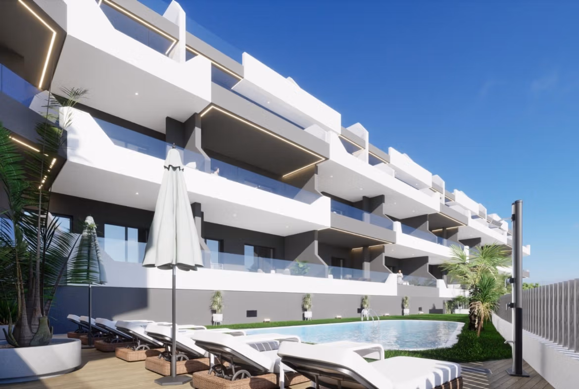 Outdoor pool and sun loungers at bright new build 2 bedroom apartment complex in Benijofar, Alicante under clear blue sky.
