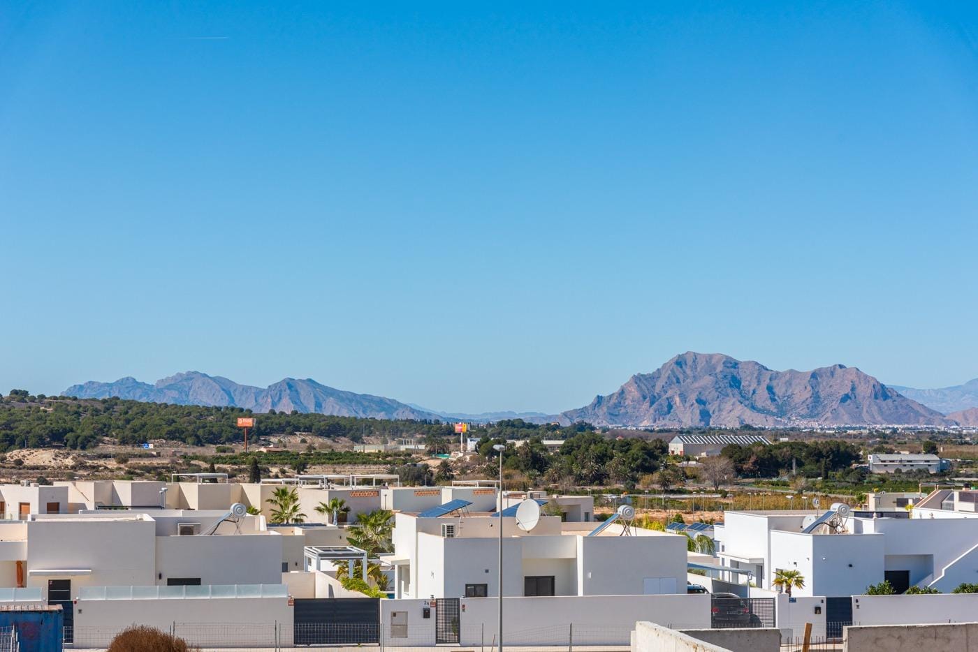 White modern buildings of the new 3 bedroom penthouse complex with solarium in Benijofar against mountain backdrop and clear sky