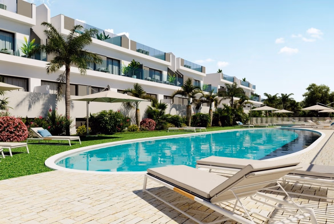 NEW-BUILD-RESIDENCIAL-IN-LOS-BALCONES-TORREVIEJA-9 Large outdoor pool with sun loungers and umbrellas in front of modern top floor apartments in Los Balcones, Torrevieja.