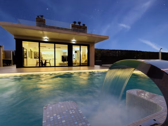 Modern new build villa in Campoamor with illuminated private pool and waterfall feature, viewed at dusk.