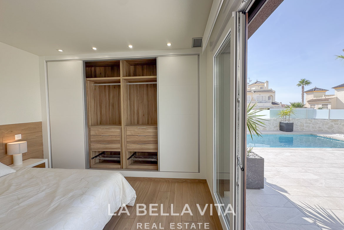 Bright, modern bedroom with built-in wardrobe and sliding doors opening to a sunlit terrace and private pool at Benijófar villa.