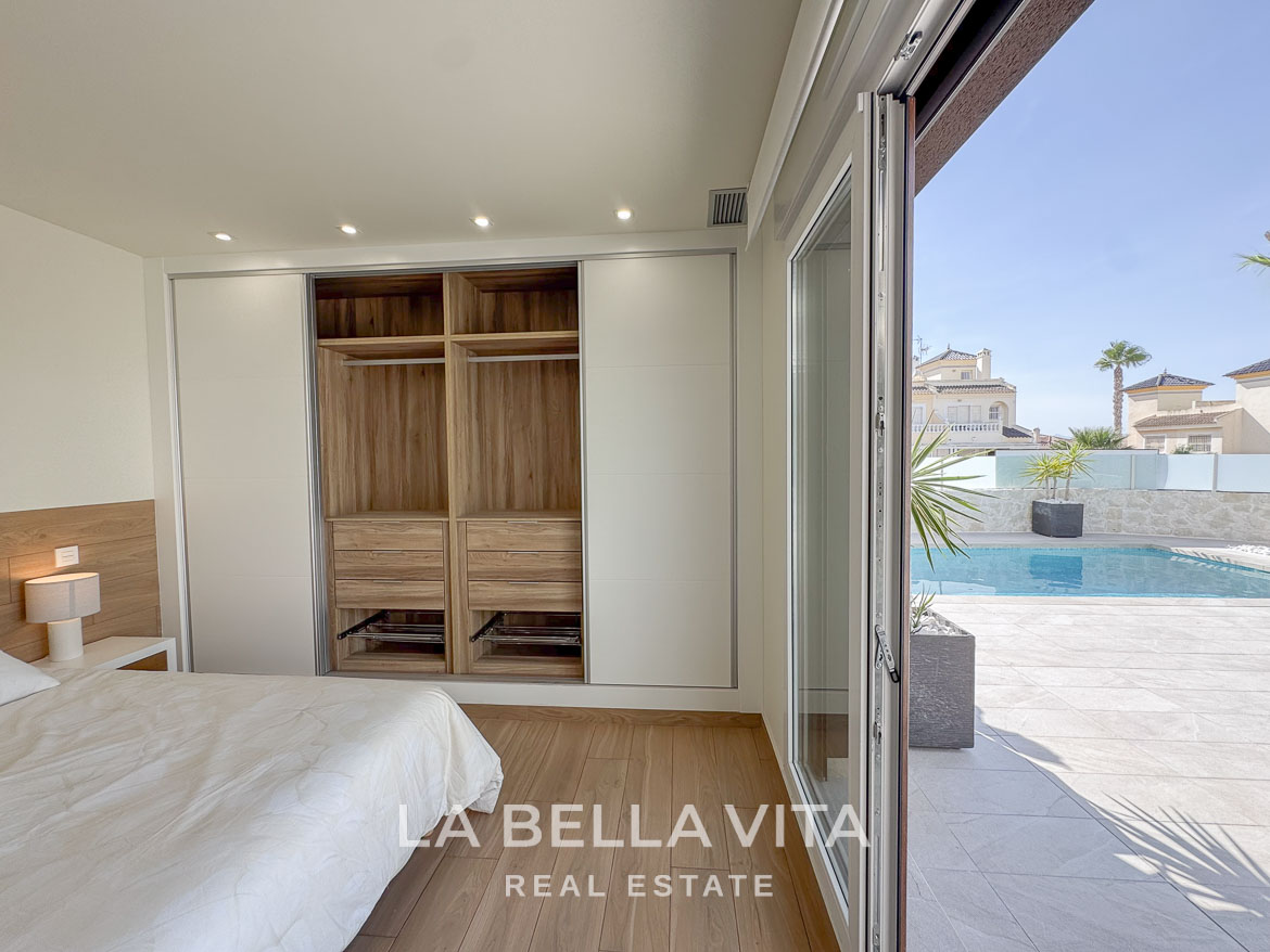 Bright, modern bedroom with built-in wardrobe and sliding doors opening to a sunlit terrace and private pool at Benijófar villa.