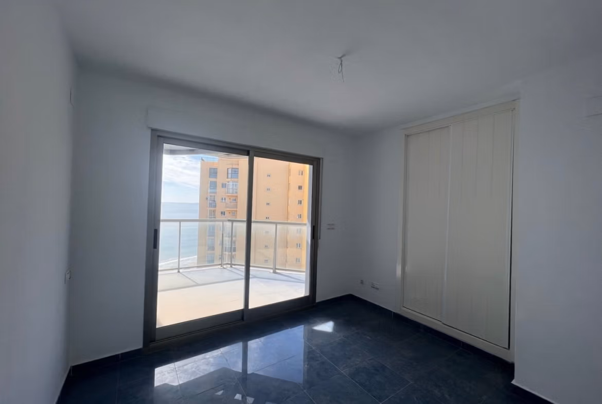 Bright, minimalist bedroom with sleek dark floors and sliding doors opening to a sea-view terrace in a Calpe penthouse.