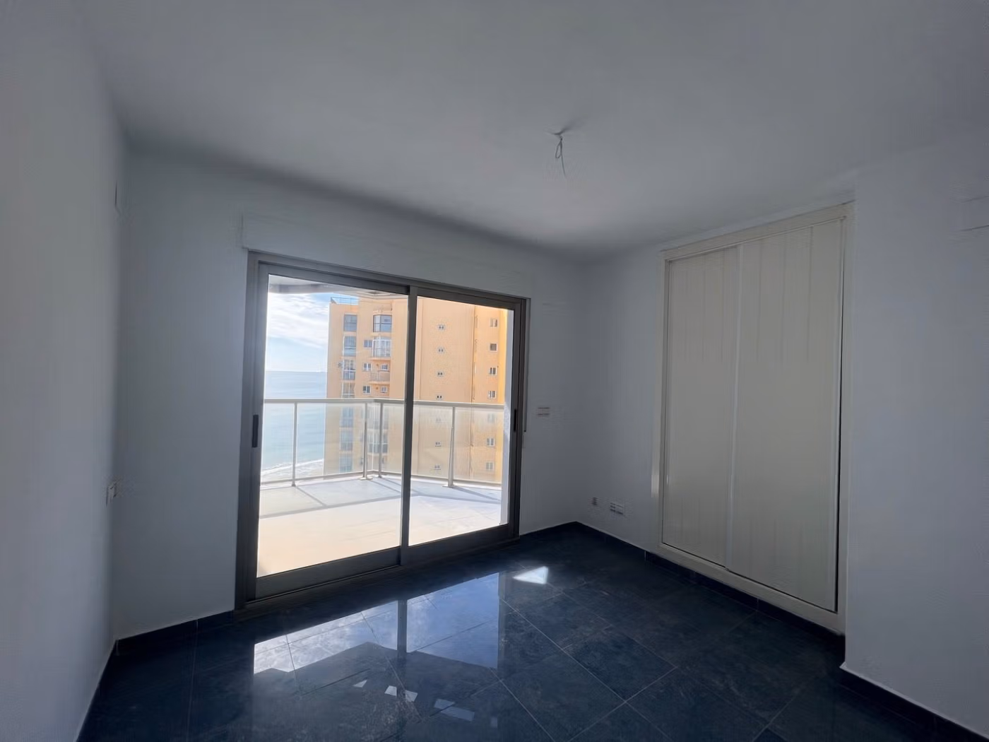 Bright, minimalist bedroom with sleek dark floors and sliding doors opening to a sea-view terrace in a Calpe penthouse.
