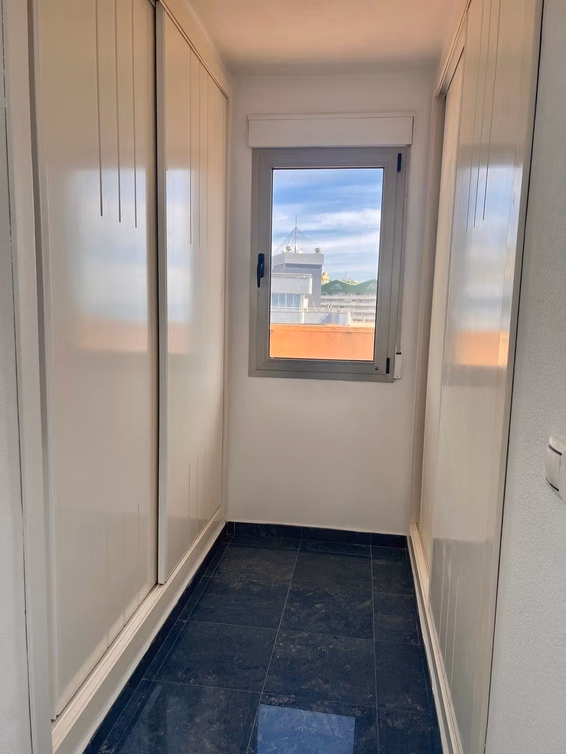 Bright and narrow walk-in closet with sleek white cabinetry in luxury 3-bedroom penthouse in Calpe.