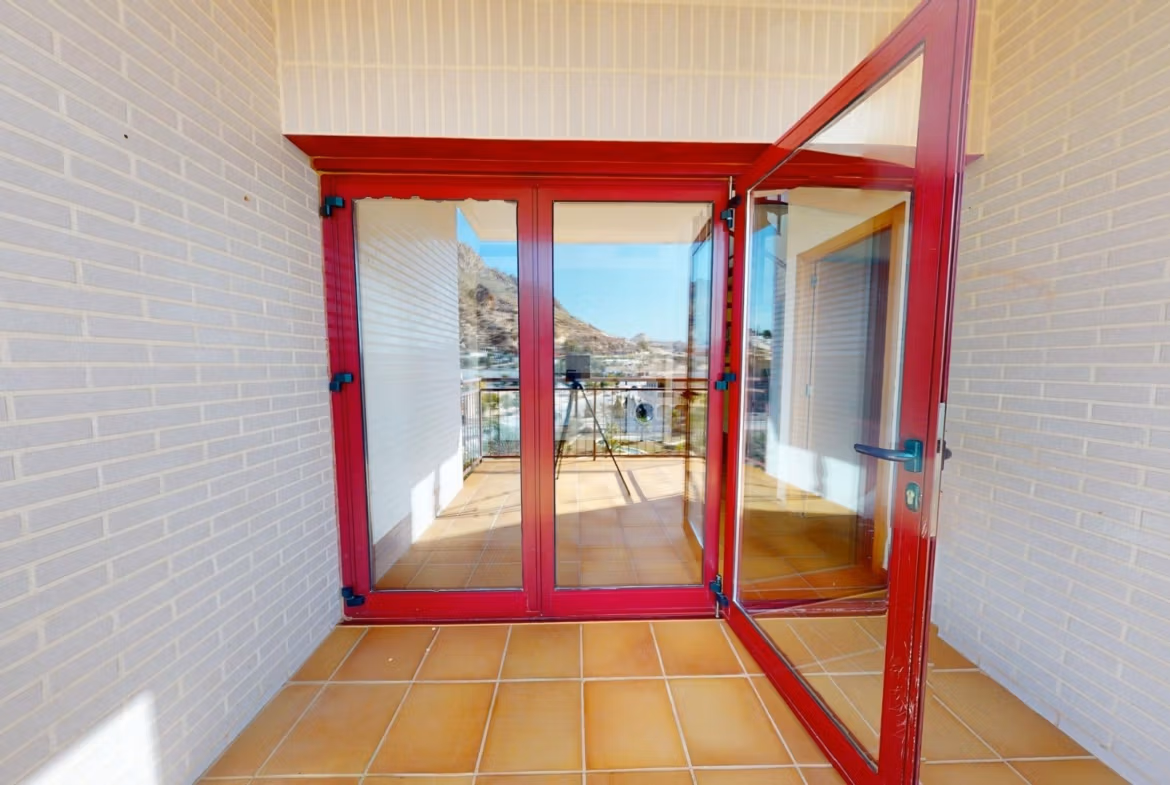 Bright private terrace with red-framed glass doors in luxury 2 bedroom penthouse near Archena, Murcia, showcasing mountain views.