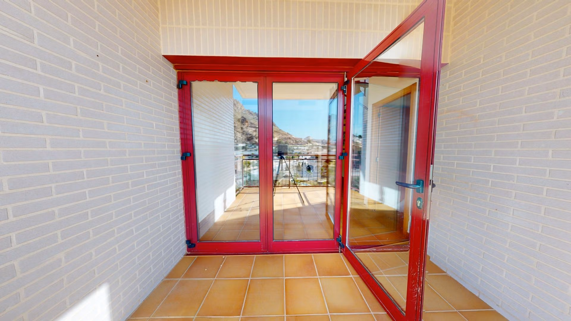 Bright private terrace with red-framed glass doors in luxury 2 bedroom penthouse near Archena, Murcia, showcasing mountain views.