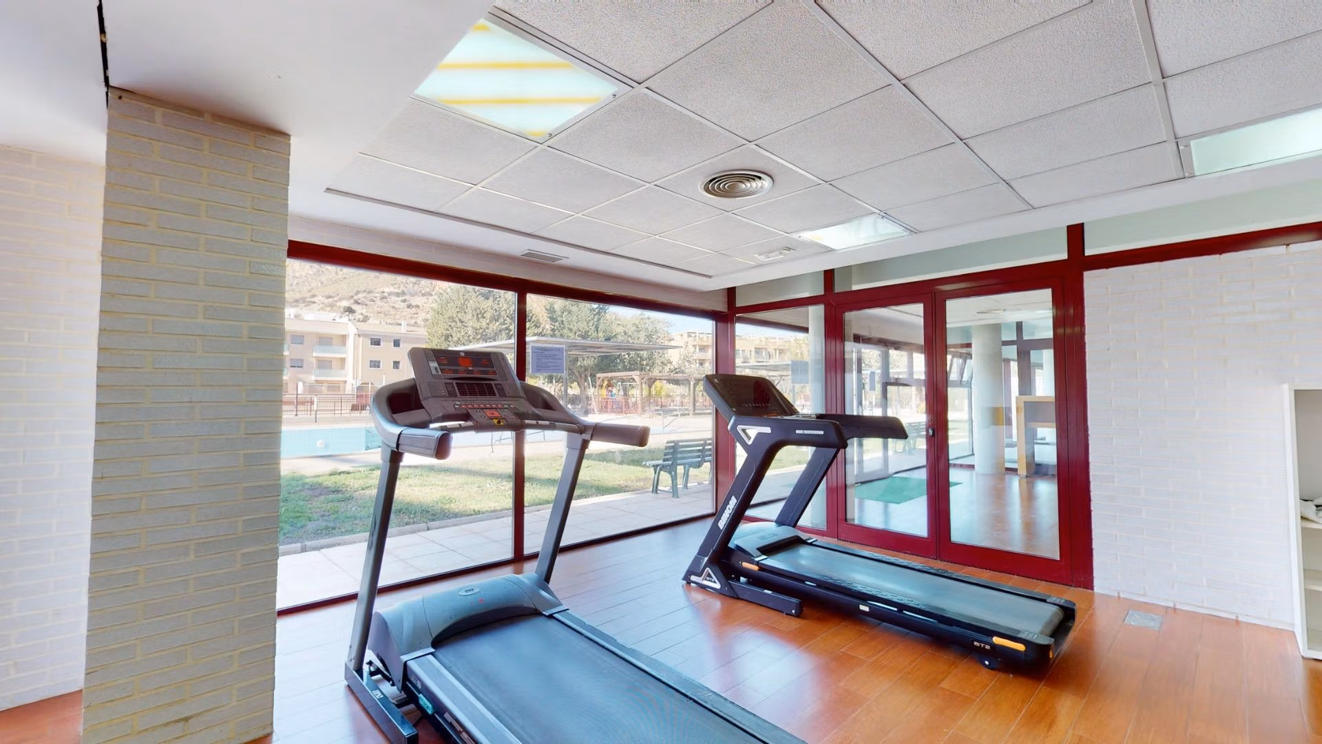 Bright, modern gym with panoramic windows overlooking the landscaped pool area in a Key Ready 1 Bedroom Apartment, Villanueva del Rio Segura.