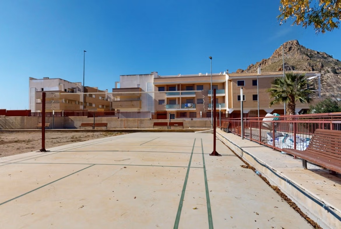 Spacious exterior view of a charming 1 bedroom apartment complex in sunny Villanueva del Rio Segura, near Archena, with mountain backdrop and sports court.