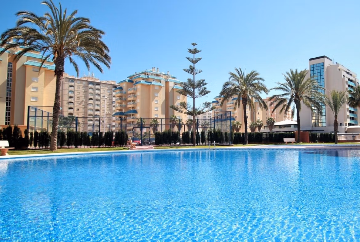 Sparkling communal pool with palm trees and modern buildings surrounding a bright new build 2-bedroom townhouse in La Manga del Mar Menor.