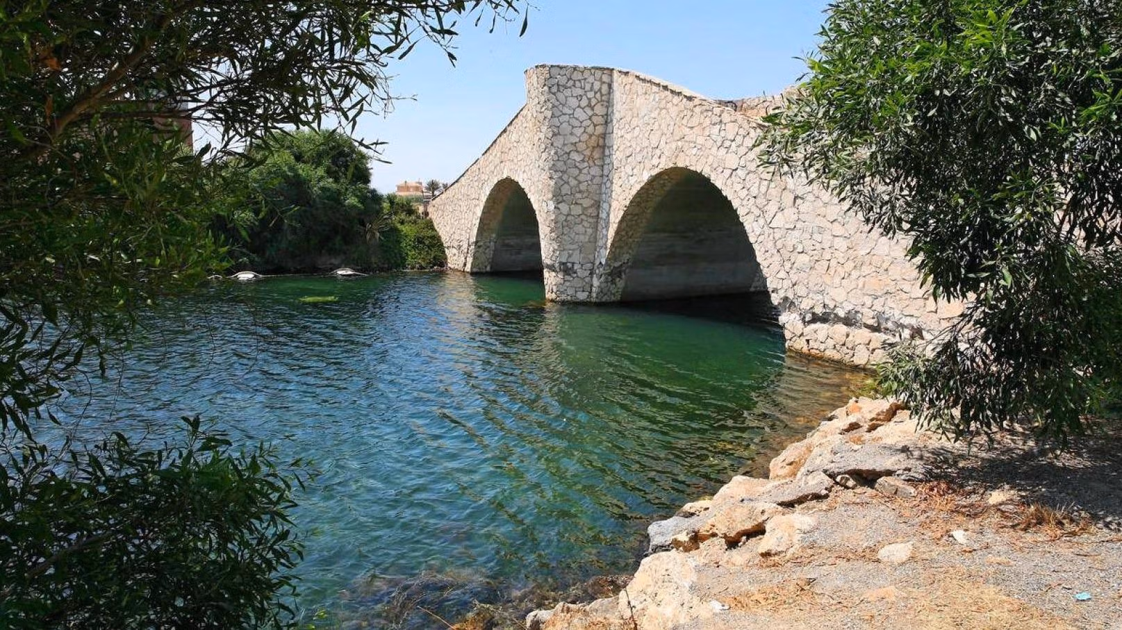 BEAUTIFUL-TOWNHOUSES-IN-LA-MANGA-16 Tranquil waterway with historic stone bridge surrounded by lush greenery near luxury townhouse in La Manga del Mar Menor