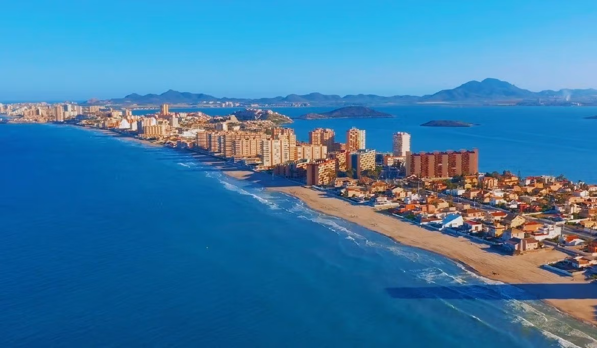 Panoramic coastal view of La Manga del Mar Menor showcasing beachfront townhouses and shimmering sea under a clear blue sky.
