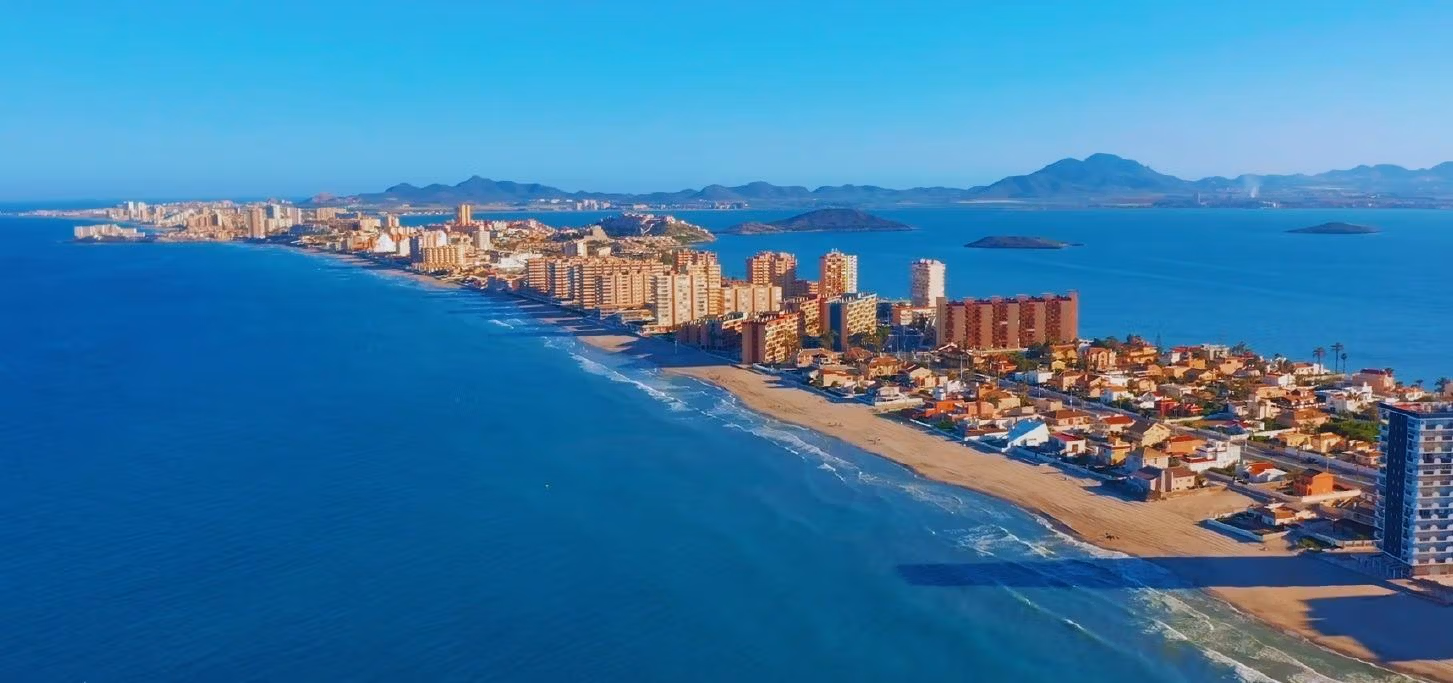 BEAUTIFUL-TOWNHOUSES-IN-LA-MANGA-17 Panoramic coastal view of La Manga del Mar Menor showcasing beachfront townhouses and shimmering sea under a clear blue sky.