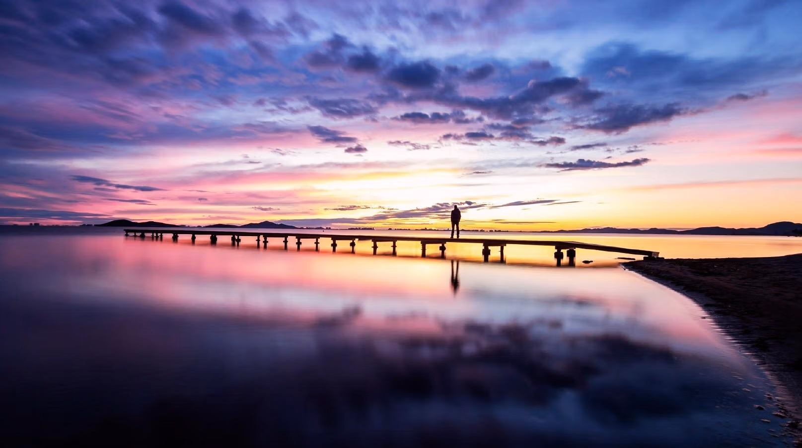 BEAUTIFUL-TOWNHOUSES-IN-LA-MANGA-21 Tranquil sunset over shimmering sea with wooden pier, highlighting serene views from a luxury townhouse in La Manga del Mar Menor.