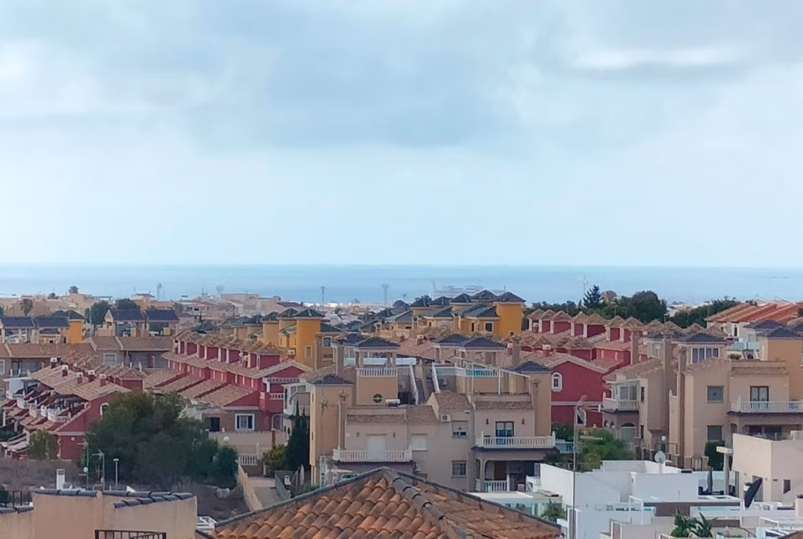Panoramic view of modern 2-bedroom townhouses with sun-drenched terraces and a glimpse of the sea in Orihuela Costa.