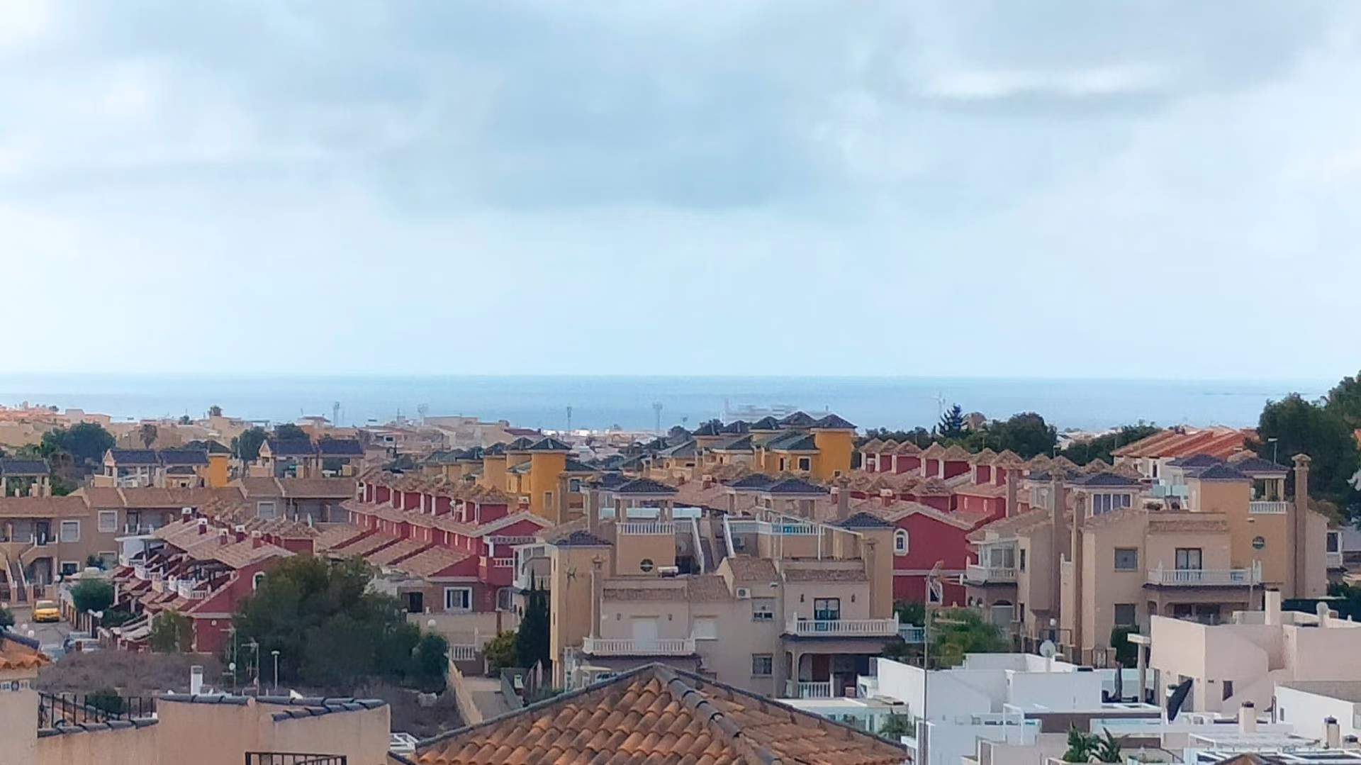 Panoramic view of modern 2-bedroom townhouses with sun-drenched terraces and a glimpse of the sea in Orihuela Costa.