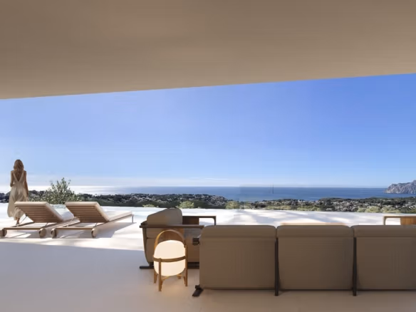 Modern architectural villa terrace en Benissa with elegant outdoor seating, sun loungers, y vistas panorámicas al mar under a clear sky.