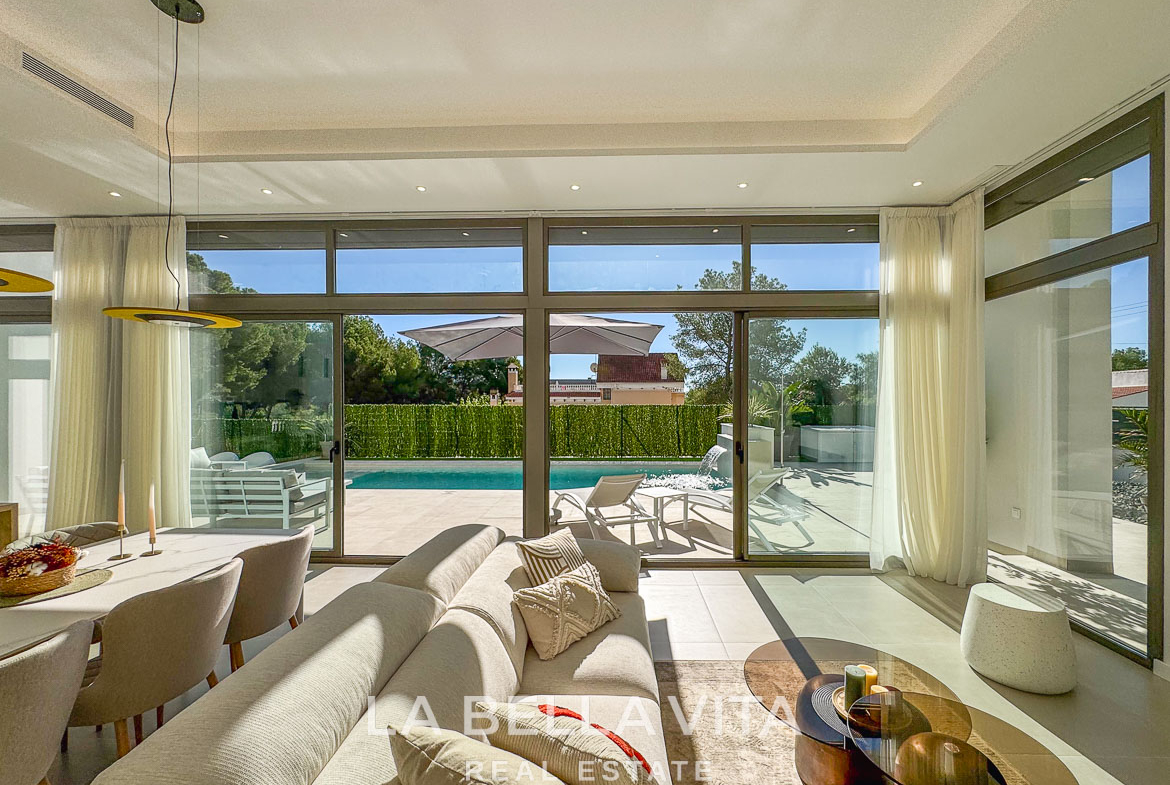 Sun-drenched open-plan living area with modern furnishings and glass doors opening to a private pool in 3-bedroom villa, Pinar de Campoverde