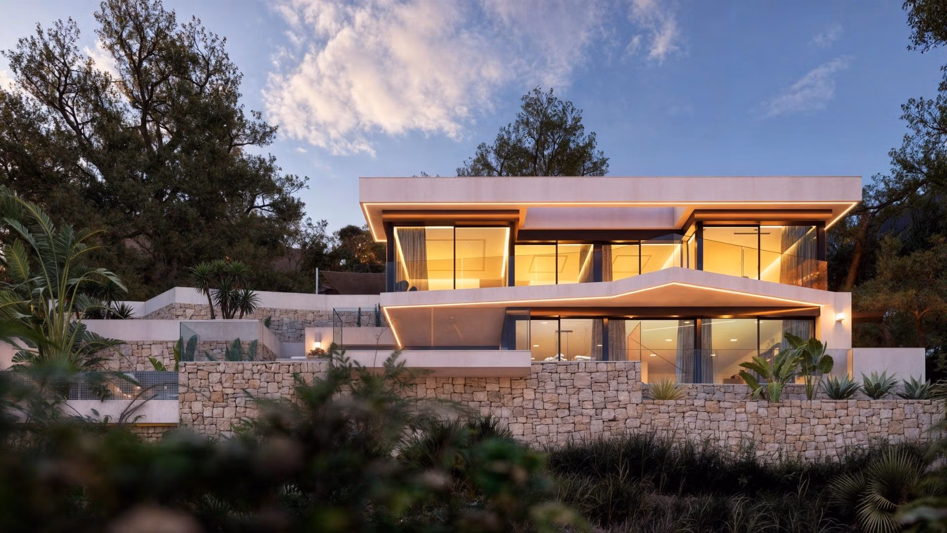 Stunning modern 4-bedroom villa in Benissa Costa with expansive glass walls, warm interior lighting, and landscaped stone terraces.