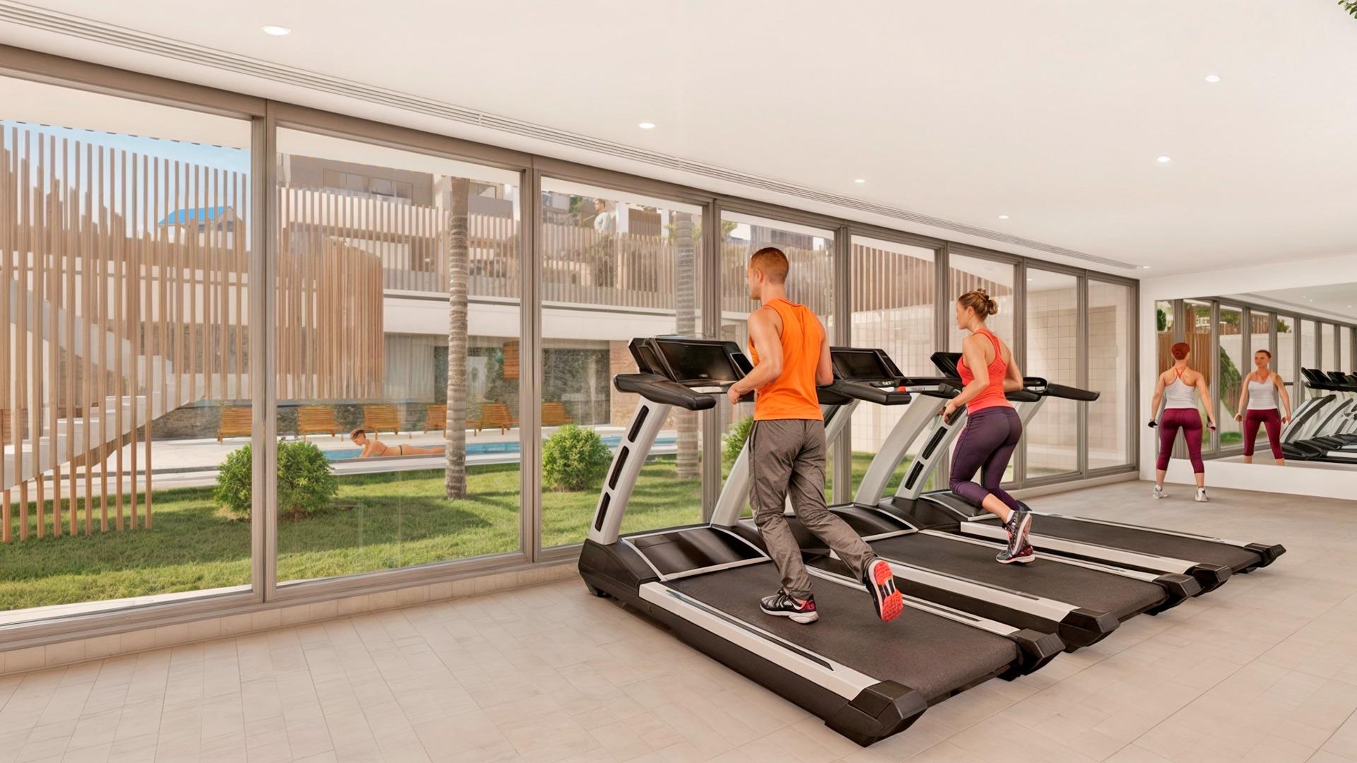 Modern gym with sunlit floor-to-ceiling windows and garden views in a stylish 3-bedroom apartment complex in Torre de la Horadada.