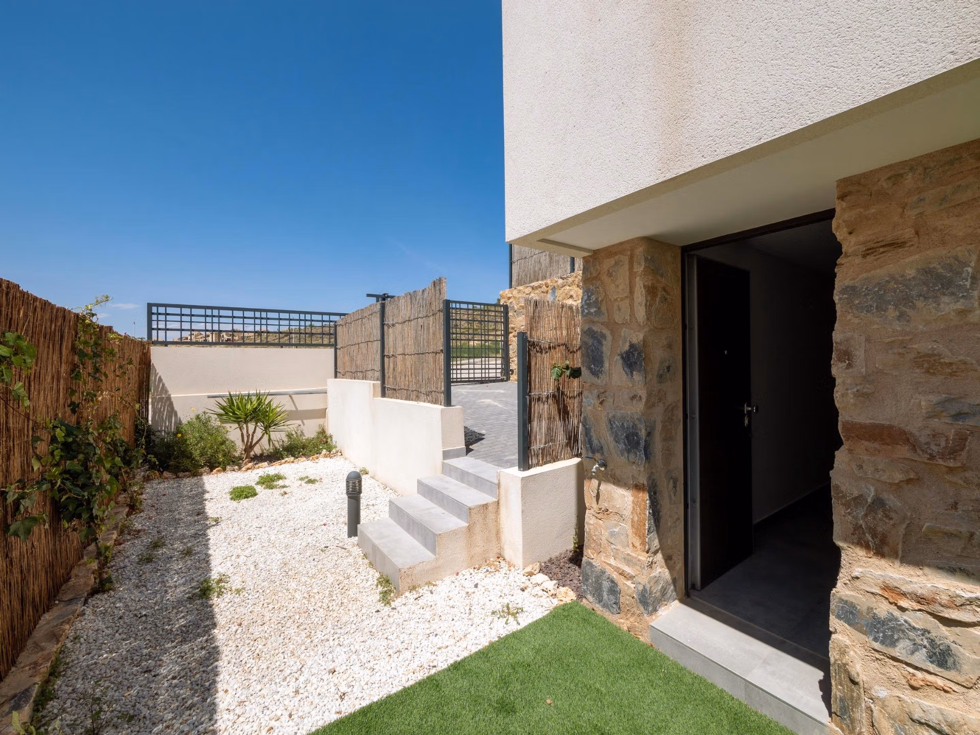Sunny modern exterior corner of a key-ready 4-bedroom villa in Algorfa with stone accents and a private garden area.