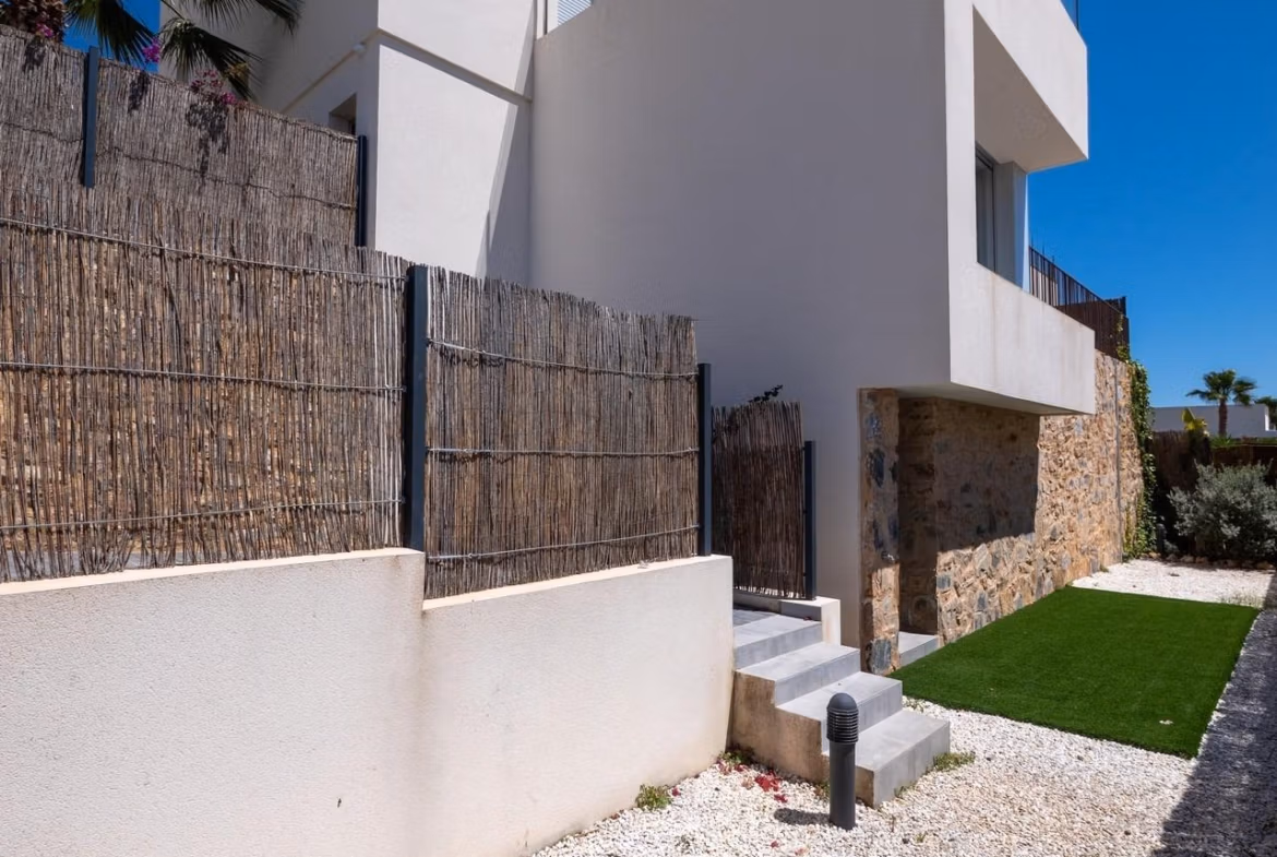 Modern whitewashed 4-bedroom villa exterior in Algorfa with sleek lines, stone accents, and landscaped gravel path under clear sky
