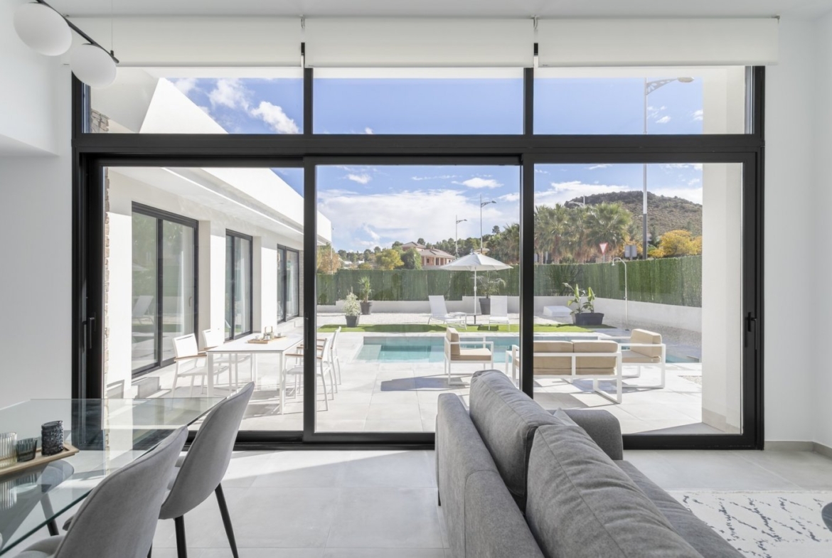 Bright open-plan living area with expansive glass doors overlooking a private pool and terrace in a modern 3-bedroom villa in Calasparra, Murcia.