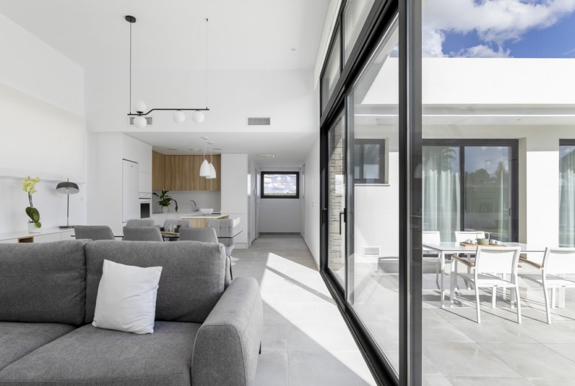 Bright open-plan living area with modern kitchen and glass doors opening to sunlit terrace in spacious 3-bedroom villa, Calasparra, Murcia.