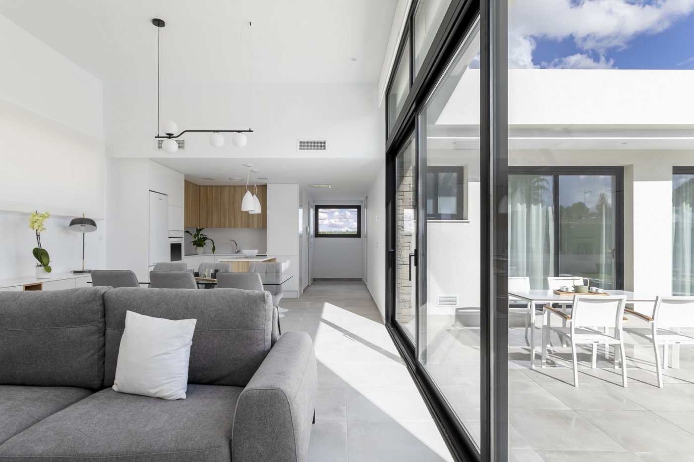 Bright open-plan living area with modern kitchen and glass doors opening to sunlit terrace in spacious 3-bedroom villa, Calasparra, Murcia.